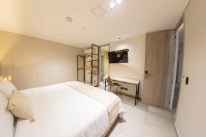 1 dormitorio con cama blanca y escritorio en Sonata 44 Hotel Laureles en Medellín