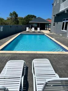 a swimming pool with two lounge chairs in front of a house at CLIFF POINT in Treasure Beach