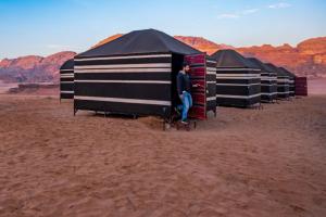 a man is standing inside a row of tents in the desert at Wadi Rum Backpacker Camp in Wadi Rum