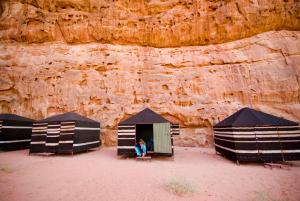 eine Person, die in einem Zelt vor einer Klippe sitzt in der Unterkunft Wadi Rum Backpacker Camp in Wadi Rum