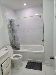 a white bathroom with a toilet and a bath tub at Langston Beautiful Home in Brampton