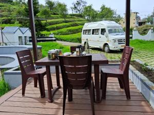 a wooden table and chairs on a deck with a van at Magizham Homestay in Kodaikānāl