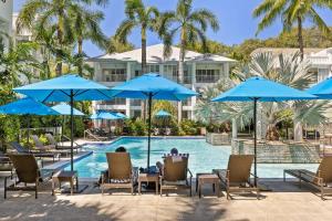 una piscina con sedie e ombrelloni blu di Fig Oasis—Poolside Resort Living at The Beach Club a Palm Cove