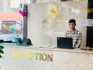 un hombre sentado en un mostrador con un portátil en Hotel Grand Bhagwat, Udaipur en Udaipur