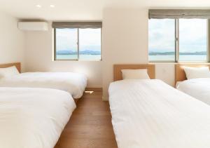 Rakuten STAY HOUSE x WILL STYLE Amakusa 105 pet allowed في Kami Amakusa: سريرين في غرفة بثلاث نوافذ