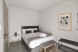 a white bedroom with a bed and a stool at Comfort City Suites & Rooms in Larisa