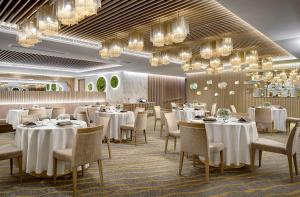um restaurante com mesas e cadeiras brancas e lustres em Nina Hotel Causeway Bay em Hong Kong