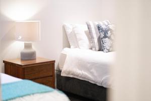 a bed with white sheets and a lamp on a night stand at Beachfront 2 in Mollymook
