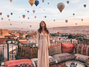 una mujer parada en un balcón con globos de aire caliente en Zara Cave Hotel en Goreme