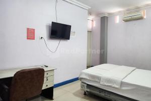 a hospital room with a bed and a desk and a tv at Puspita Homestay Mitra RedDoorz in Jakarta