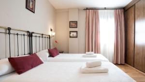 a bedroom with two beds with white sheets and red pillows at Hospederia Princesa Elima in Brihuega