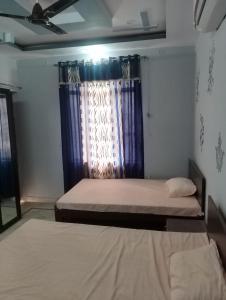 a bedroom with two beds and a window with blue curtains at Comfort Inn Guesthouse in Jaipur