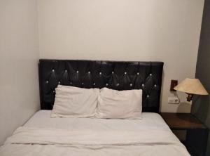 1 cama con cabecero negro y almohadas blancas en Gangnam Style Residence Mitra RedDoorz near MERR Surabaya, en Surabaya