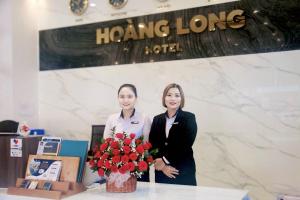 twee vrouwen die naast een tafel staan met een vaas met bloemen bij Hoang Long Hotel Phan Thiết in Phan Thiet