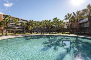 a large swimming pool with palm trees in front of a building at Hopstays - Vila das Lagoas - Salgados in Albufeira