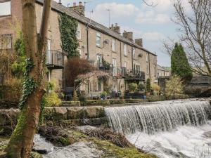 a waterfall in front of houses next to a river at Bear Pit Cottage in Hayfield