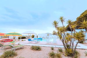 Resort Giglio di Mare في سيليا مارينا: مسبح مع كراسي ومظلات على الشاطئ