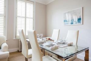 comedor con mesa de cristal y sillas blancas en Elm Park Apartment - 2 Bed Chelsea Apartment, en Londres