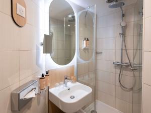 uma casa de banho com um lavatório e um chuveiro com um espelho. em Mercure Paris Notre Dame Saint Germain des Prés em Paris