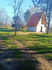 a white barn with a red roof in a field at Vikendica Kelebija in Subotica