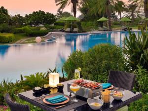 - une table avec de la nourriture et des boissons à côté de la piscine dans l'établissement Mövenpick Hotel Bahrain, à Manama