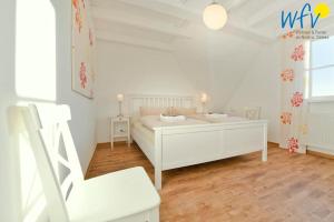 una camera da letto bianca con un letto e una sedia di Landhaus Ostdüne Ferienwohnung Dünenmeer a Juist