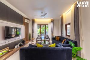 カルジャットにあるStayVista's The Isabella House - Hill-View Villa with Outdoor Pool & Pool-Side Gazeboの青いソファとテレビのあるリビングルーム