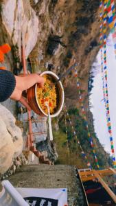 uma pessoa segurando uma xícara de comida na frente de uma montanha em Rivulet Resort & Camping em Mussoorie