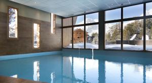 einen Pool mit Blick auf ein Haus durch Fenster in der Unterkunft Hôtel Club mmv Altitude **** in Arc 2000