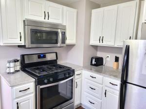 cocina con armarios blancos, fogones y microondas en Apartment with Brand new furniture and large parking, en West Seneca