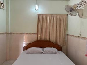 uma cama com 2 almofadas e uma janela com uma ventoinha em Palm Tree Quest House em Battambang