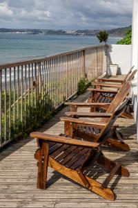 Inn on the Shore في Downderry: صف من الكراسي الخشبية تجلس على شرفة مطلة على المحيط