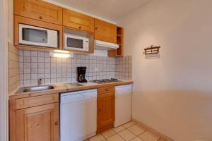 eine Küche mit Holzschränken, einer Spüle und einer Mikrowelle in der Unterkunft Cabourg - 33 - Studio bonne expo - 4 pers in Les Deux Alpes