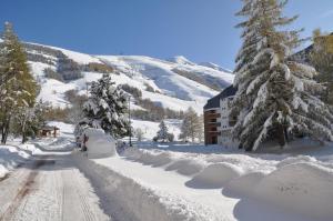 eine schneebedeckte Straße mit Bäumen und einem Gebäude in der Unterkunft Cabourg - 33 - Studio bonne expo - 4 pers in Les Deux Alpes