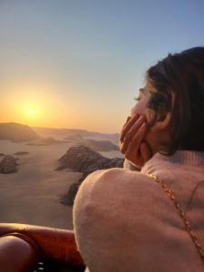 a woman sitting on the edge of a mountain looking at the sunset at Wadi Rum Nabatean Camp in Wadi Rum