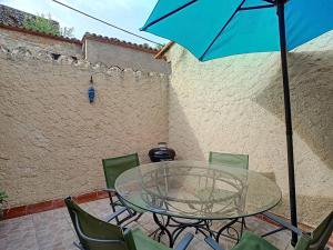 a glass table and chairs with a blue umbrella at Le Temps Suspendu - Maison atypique avec terrasse in Fitou