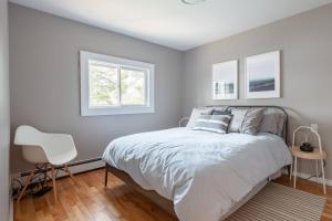a white bedroom with a bed and a white chair at Dreamy Lakefront View Retreat House on Melissa Ave in Terence Bay
