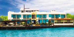 a large white building with blue windows next to the water at Hotel Solymar in Puerto Ayora