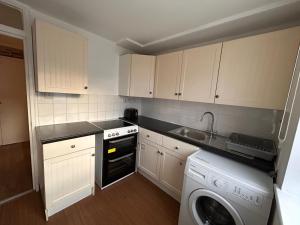 a small kitchen with white cabinets and a dishwasher at Spacious one bed flat in eastlondon with parking and free wifi in Goodmayes