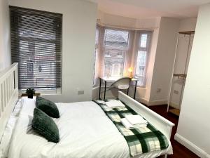 a white bed with green pillows in a room with windows at Stratford Guesthouse in London