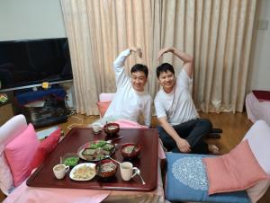 Dois homens sentados numa sala com uma bandeja de comida. em 8-17 Nomura Motomachi - House / Vacation STAY 1894 em Hirakata