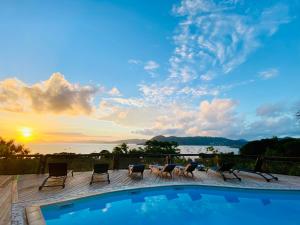 a pool with chairs and a sunset in the background at Anoli Lodges in Sainte-Anne