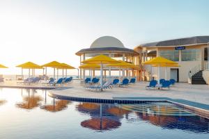Pickalbatros Vita Resort - Portofino Marsa Alam في أبو دباب: مسبح مع كراسي ومظلات أمام المبنى