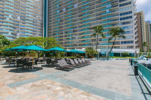 eine Terrasse mit Stühlen und Sonnenschirmen vor einem großen Gebäude in der Unterkunft Ilikai Tower 333 Yacht Harbor View 1BR in Honolulu