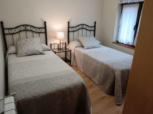 1 dormitorio con 2 camas, lámpara y ventana en Apartamentos Carolina, en Celorio