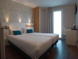 a bedroom with a large white bed with blue pillows at Brit Hotel Les Alizes in Pornic