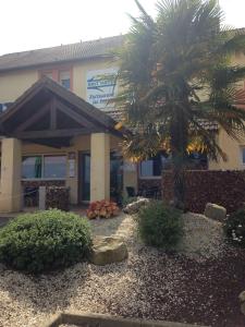 a building with a palm tree in front of it at Brit Hotel Les Evens in Saint-Saturnin