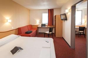 モントーバンにあるBrit Hotel Confort Montaubanのベッド、ソファ、デスクが備わるホテルルームです。