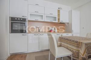 a kitchen with white cabinets and a table with a chair at Simple Apartment in Prishtinë