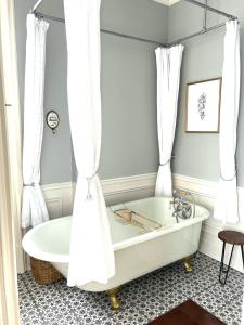 a bathtub in a bathroom with white curtains at La Demeure du Capitaine in Neuville